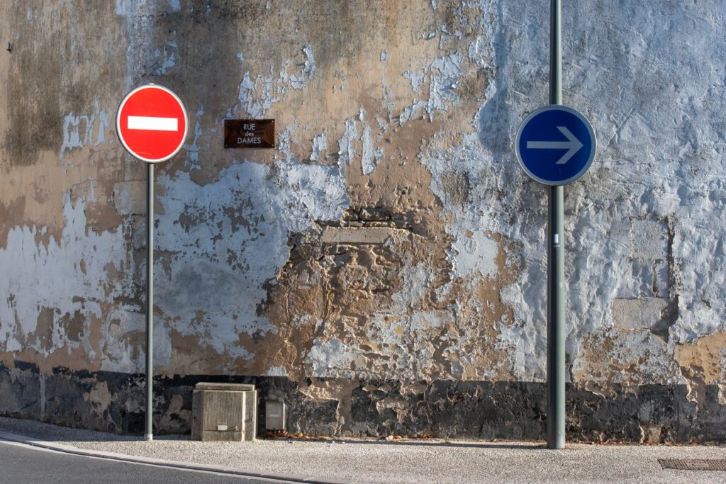 Signage against a weathered wall in an urban setting with directional arrows.